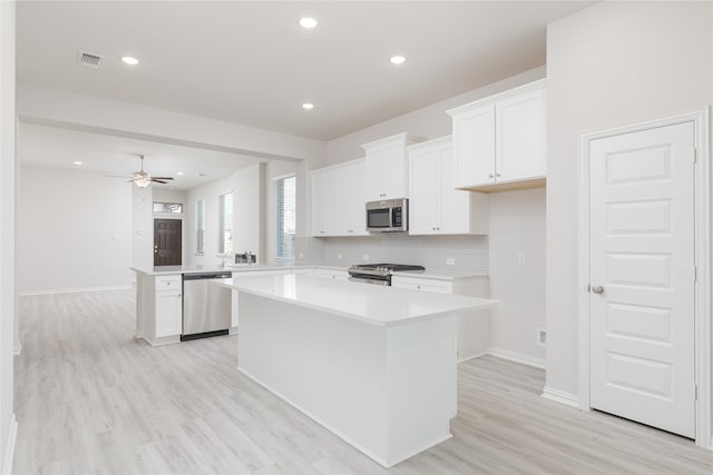 kitchen with white cabinets, decorative backsplash, a kitchen island, appliances with stainless steel finishes, and light hardwood / wood-style flooring