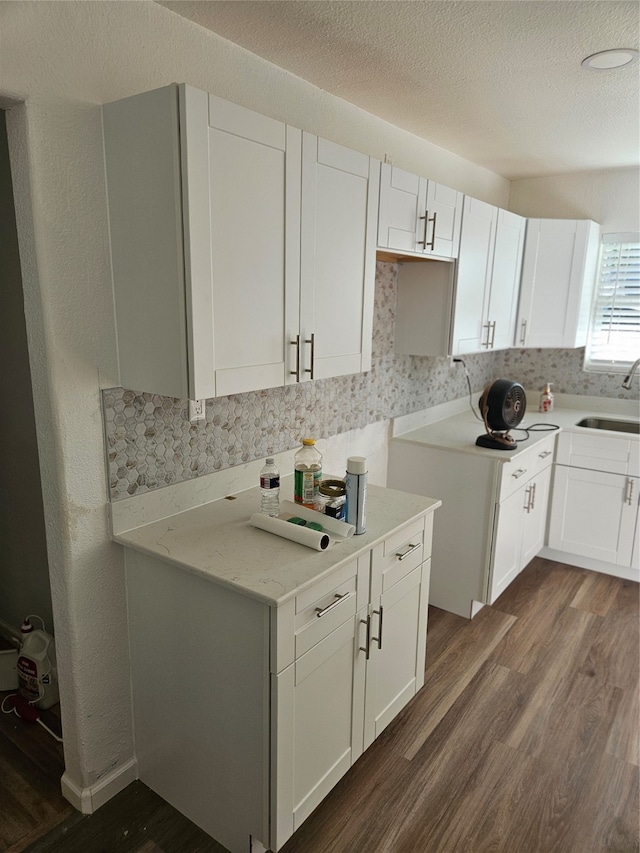 kitchen with light stone counters, white cabinetry, sink, and dark wood-type flooring