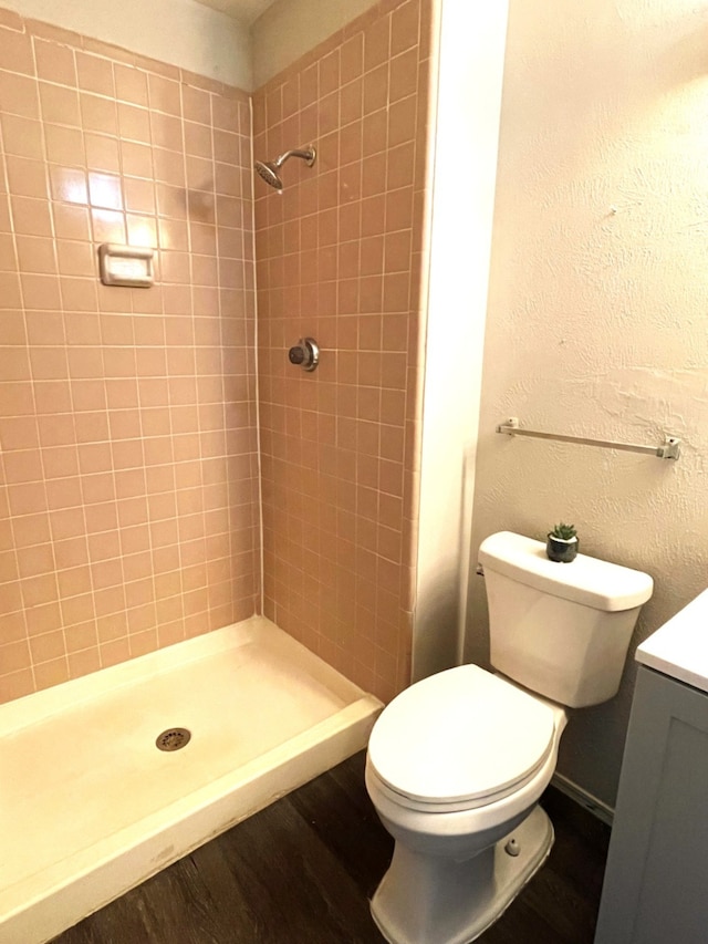 bathroom featuring a tile shower, hardwood / wood-style flooring, toilet, and vanity