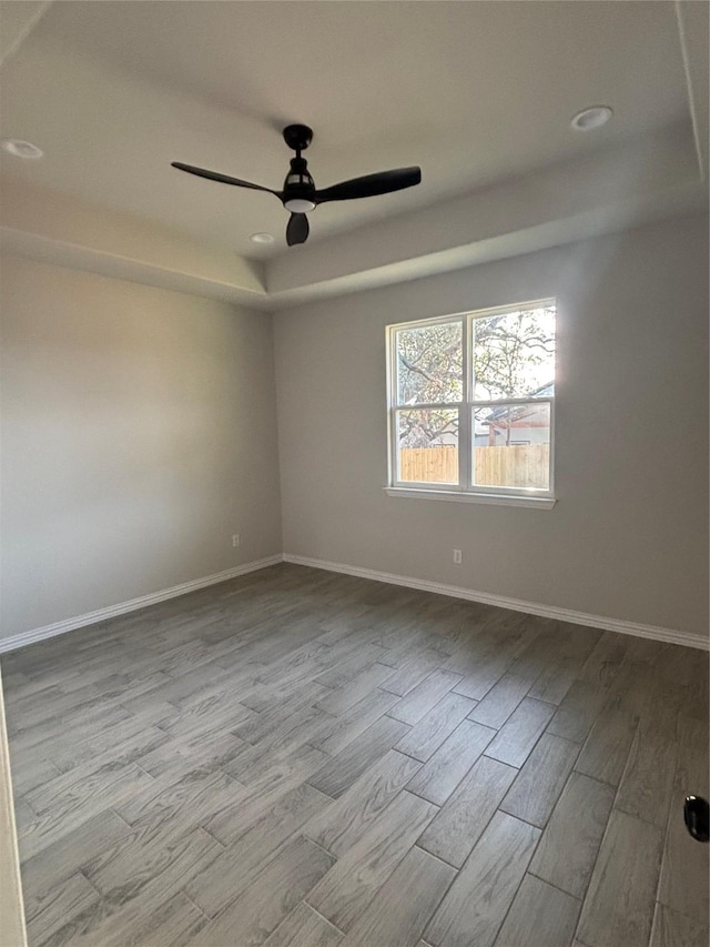 empty room with a tray ceiling, ceiling fan, and light hardwood / wood-style flooring