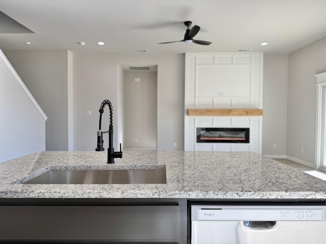 kitchen with dishwashing machine, sink, ceiling fan, and light stone countertops