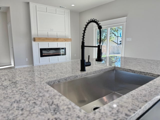 kitchen with light stone counters, white cabinetry, and sink