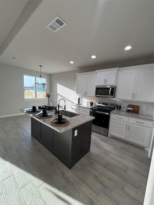 kitchen with white cabinets, sink, stainless steel appliances, and an island with sink