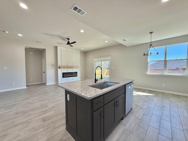 kitchen featuring light stone counters, ceiling fan with notable chandelier, sink, dishwasher, and an island with sink