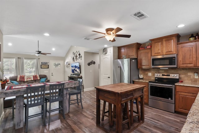 kitchen with tasteful backsplash, light stone counters, stainless steel appliances, dark hardwood / wood-style floors, and lofted ceiling