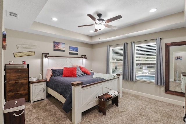 carpeted bedroom with ceiling fan and a raised ceiling