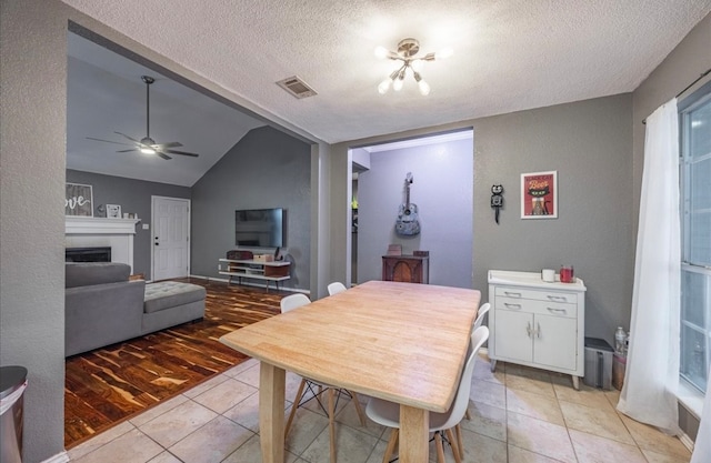 dining space with ceiling fan, lofted ceiling, a textured ceiling, light hardwood / wood-style flooring, and a tiled fireplace