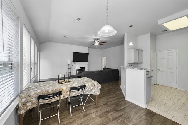 kitchen with ceiling fan, pendant lighting, wood-type flooring, light stone counters, and backsplash