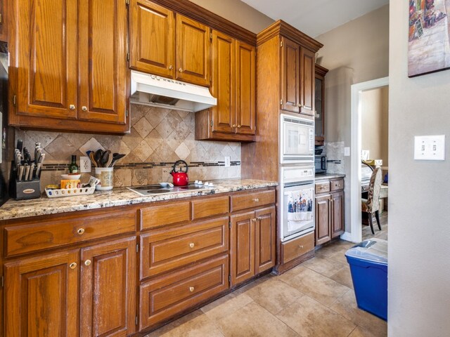 kitchen featuring decorative backsplash, white appliances, light tile patterned flooring, and light stone countertops