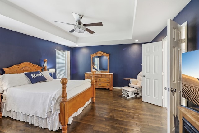 bedroom featuring hardwood / wood-style floors, a tray ceiling, baseboards, and ceiling fan