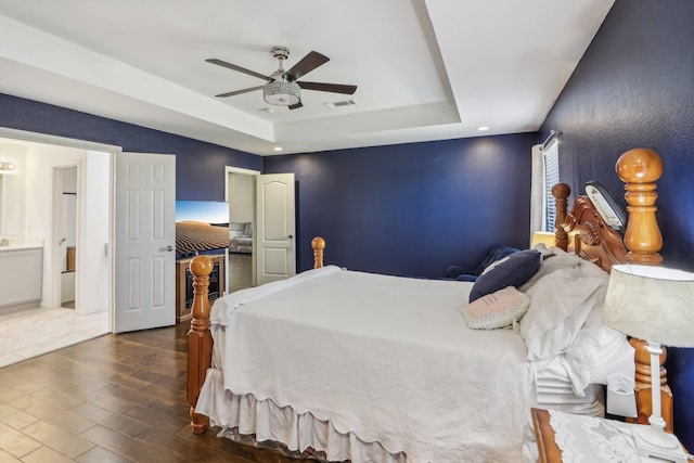 bedroom featuring ensuite bathroom, visible vents, ceiling fan, a raised ceiling, and dark wood finished floors