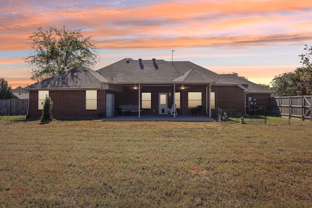 back house at dusk featuring a lawn and a patio