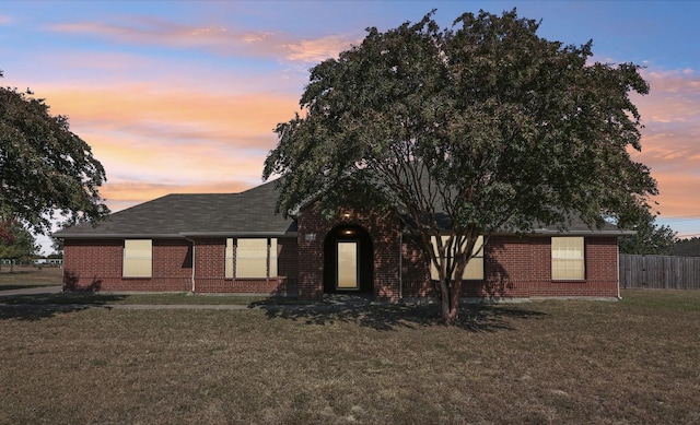 view of front of property with a lawn, fence, and brick siding