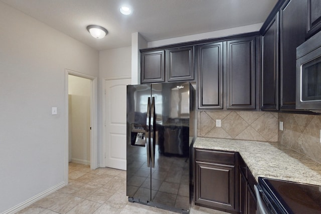 kitchen with decorative backsplash, light stone countertops, black fridge, light tile patterned floors, and range