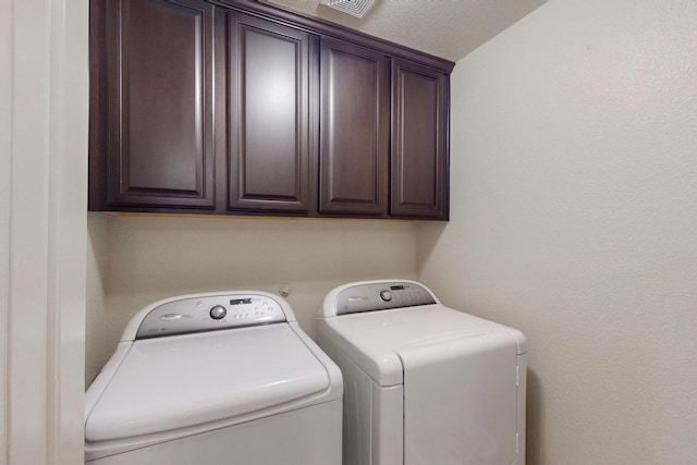 clothes washing area with washer and clothes dryer, cabinets, and a textured ceiling