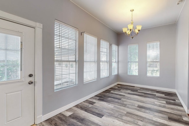 unfurnished dining area with hardwood / wood-style flooring, crown molding, and an inviting chandelier