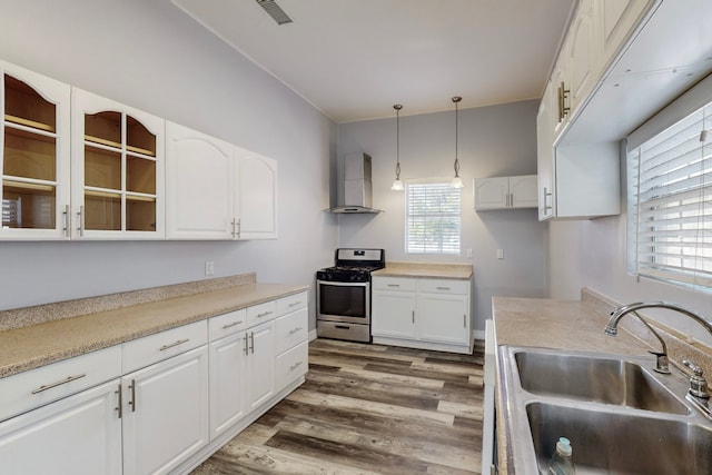 kitchen featuring wall chimney exhaust hood, hanging light fixtures, gas range, and white cabinets