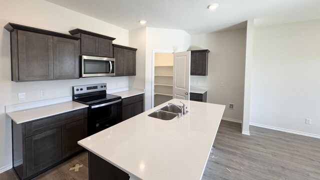 kitchen with appliances with stainless steel finishes, dark brown cabinets, dark wood-type flooring, sink, and a center island with sink