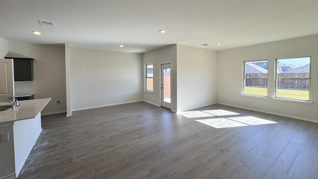 unfurnished living room featuring sink, dark wood-type flooring, and a wealth of natural light