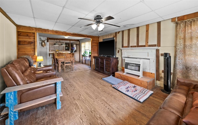 living room with ceiling fan, heating unit, wood-type flooring, and a paneled ceiling