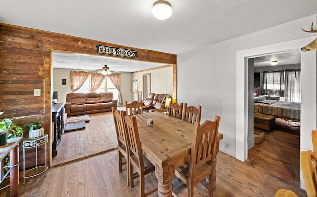 dining space featuring ceiling fan, wood-type flooring, and wooden walls