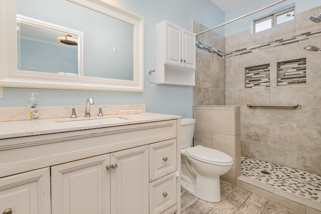 bathroom with toilet, tiled shower, and vanity