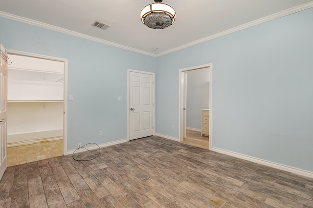 unfurnished bedroom featuring wood-type flooring, a closet, crown molding, and a spacious closet