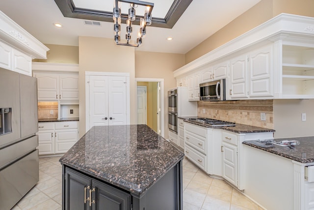 kitchen with appliances with stainless steel finishes, a kitchen island, white cabinetry, and decorative light fixtures