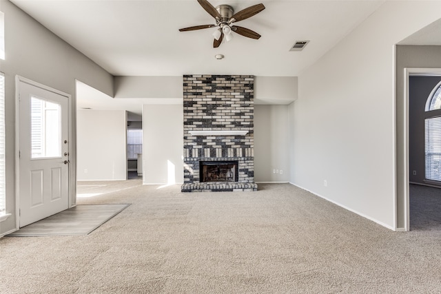 unfurnished living room featuring a brick fireplace, ceiling fan, a wealth of natural light, and light carpet