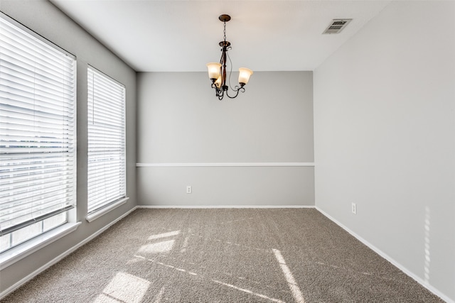 carpeted spare room featuring an inviting chandelier