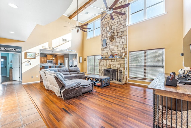 living room featuring a stone fireplace, beamed ceiling, hardwood / wood-style floors, and high vaulted ceiling