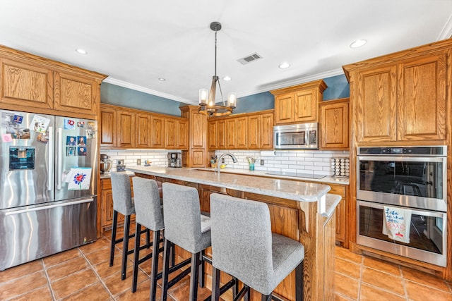 kitchen with an island with sink, decorative light fixtures, backsplash, appliances with stainless steel finishes, and a breakfast bar