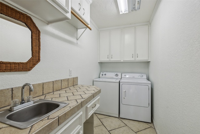 clothes washing area with light tile patterned flooring, sink, a textured ceiling, cabinets, and separate washer and dryer