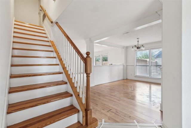 staircase featuring hardwood / wood-style flooring, decorative columns, and a chandelier