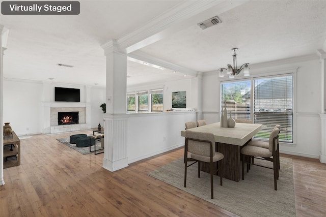 dining space featuring light hardwood / wood-style floors, a chandelier, ornamental molding, and decorative columns