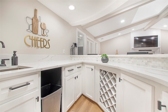 kitchen featuring lofted ceiling with beams, light wood-type flooring, tasteful backsplash, light stone counters, and sink