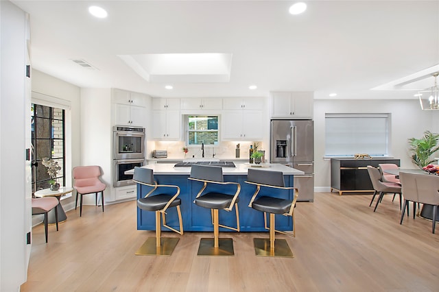 kitchen featuring white cabinets, light hardwood / wood-style floors, stainless steel appliances, a center island, and a kitchen bar