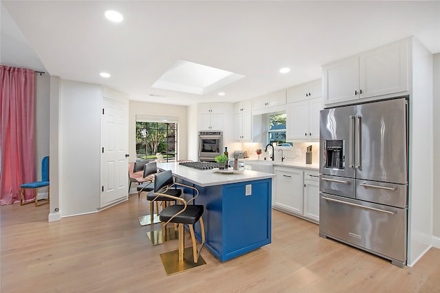 kitchen featuring light wood-type flooring, a kitchen island, a breakfast bar, stainless steel appliances, and white cabinets