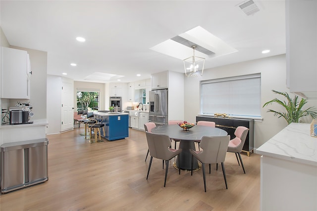 dining space with a skylight, an inviting chandelier, sink, and light hardwood / wood-style floors