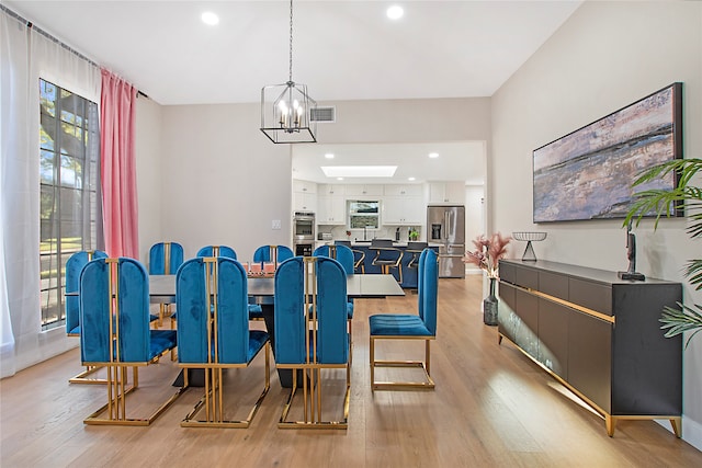 dining space with a skylight, a chandelier, and light wood-type flooring