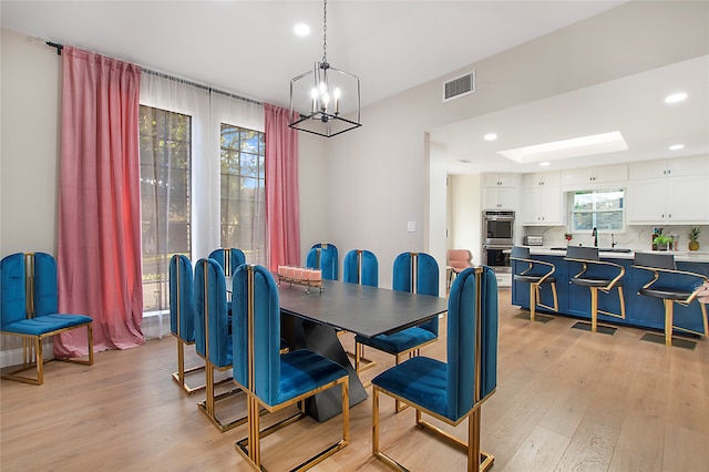 dining space with light wood-type flooring, sink, and a chandelier