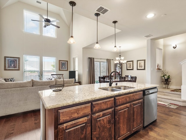 kitchen with light stone counters, dark wood-type flooring, sink, a center island with sink, and dishwasher