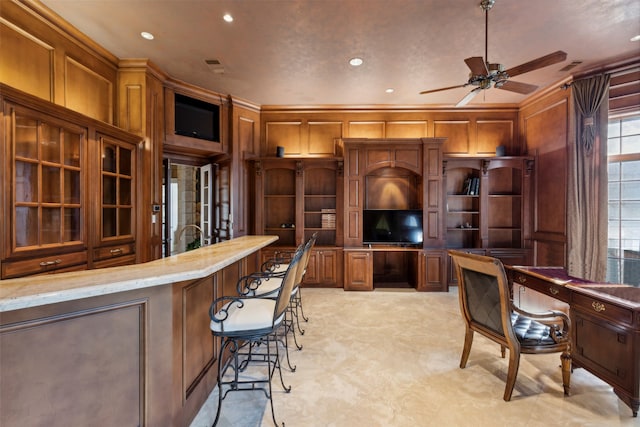 kitchen featuring crown molding, light stone counters, a breakfast bar, and ceiling fan