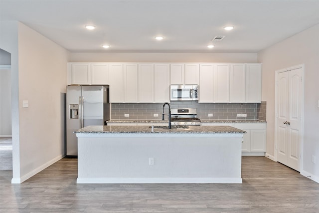 kitchen with stainless steel appliances, white cabinetry, a kitchen island with sink, and dark stone counters