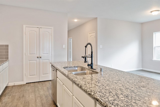 kitchen featuring light wood-type flooring, light stone counters, stainless steel dishwasher, and sink