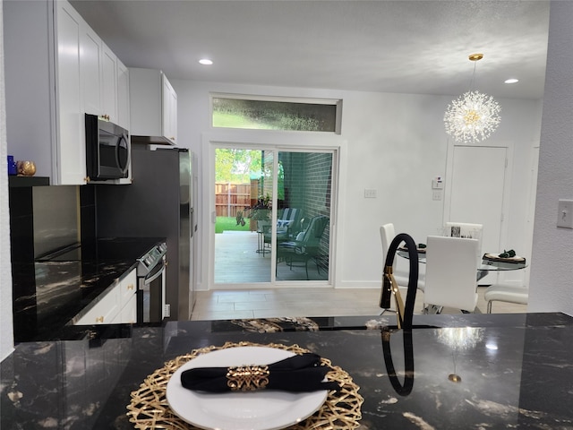 kitchen with dark stone countertops, white cabinets, stainless steel appliances, and hanging light fixtures