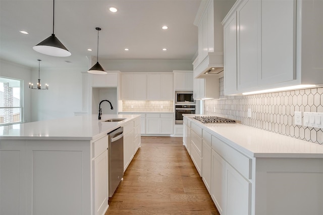 kitchen with sink, a large island with sink, white cabinetry, appliances with stainless steel finishes, and crown molding