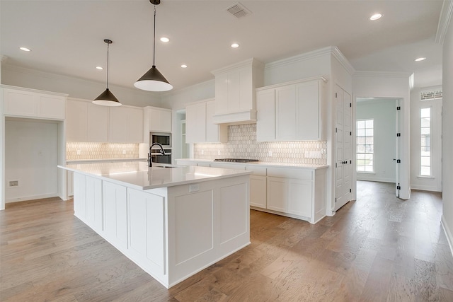 kitchen featuring an island with sink, sink, white cabinetry, stainless steel appliances, and light hardwood / wood-style floors