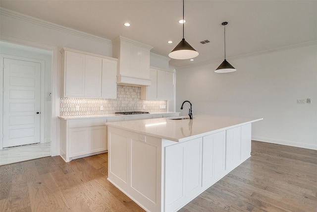 kitchen with a center island with sink, light wood-type flooring, sink, and white cabinets