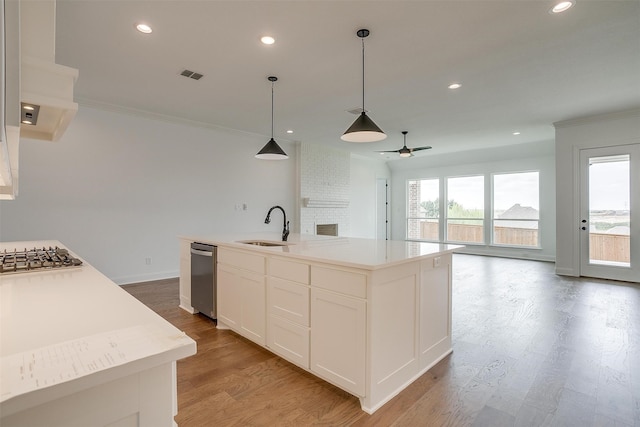 kitchen featuring light wood-type flooring, white cabinets, sink, a center island with sink, and decorative light fixtures